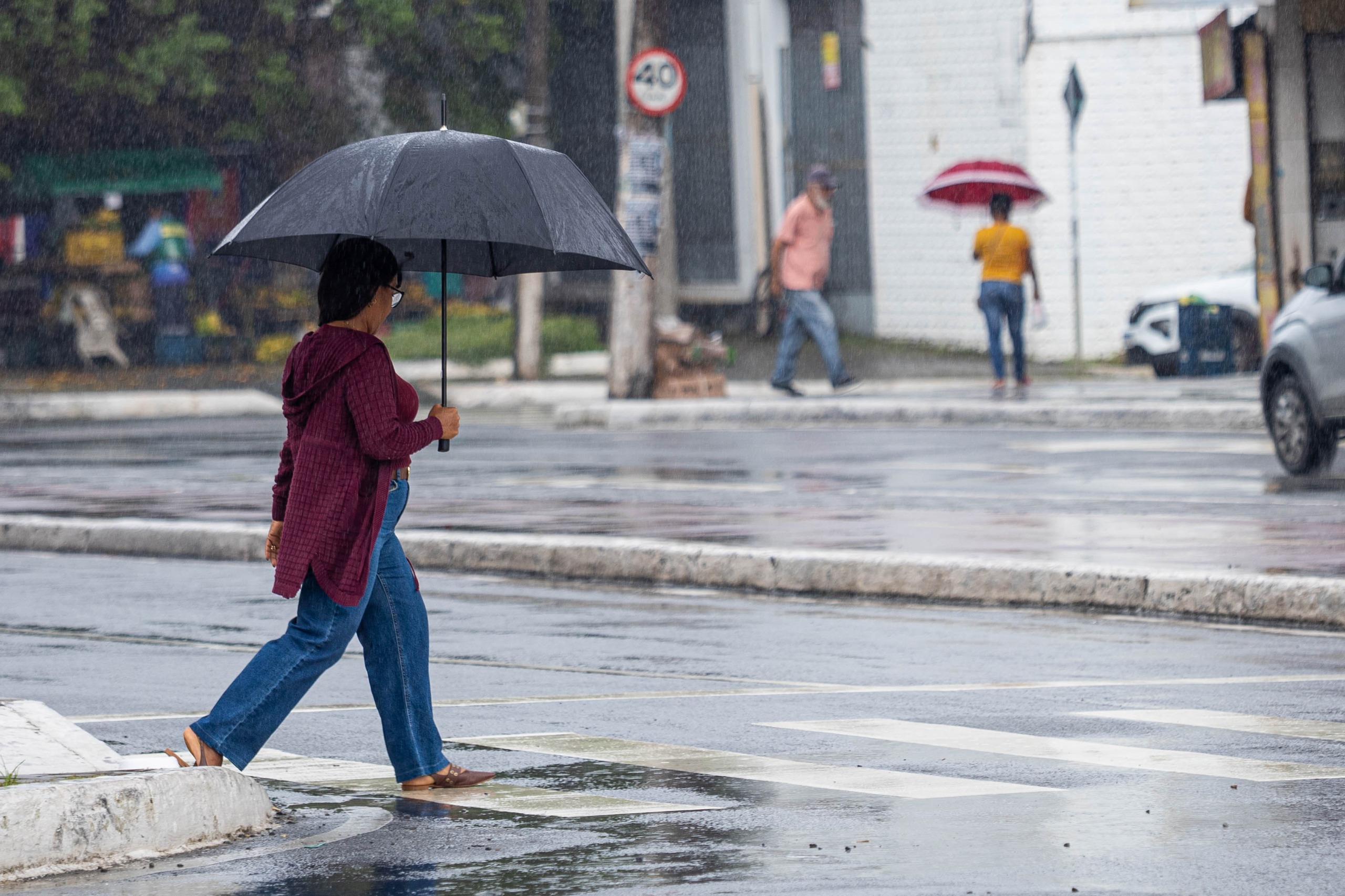 Pedestre atravessa rua sob chuva durante alerta laranja para chuva em Camaçari