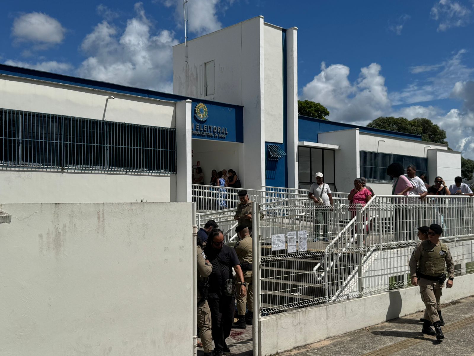 Fórum Eleitoral de Camaçari com policiais e pessoas na área externa após ocorrência que deixou um homem morto e um vigilante ferido.