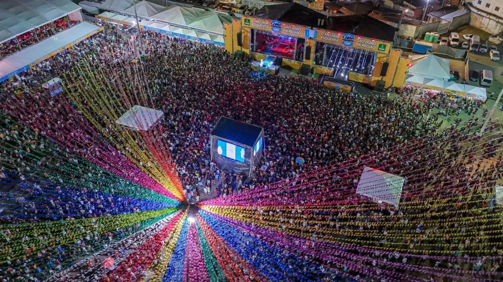 Vista aérea do Camaforró 2024 com grande público e bandeirolas coloridas em Camaçari.